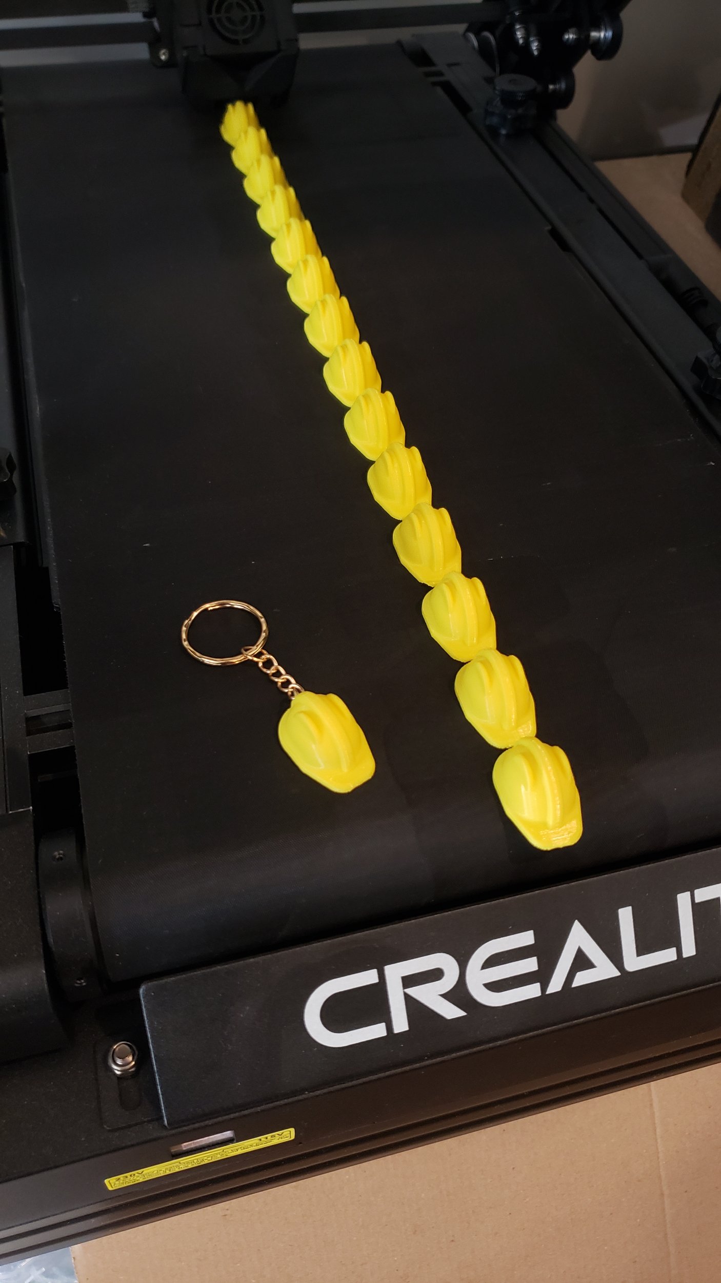 Gros plan sur une imprimante 3D avec un Z infini qui est un tapis roulant. Sur l'imprimante, une ligne d'impression avec une multitude de petits casques réalisé grâce à cette machine.
