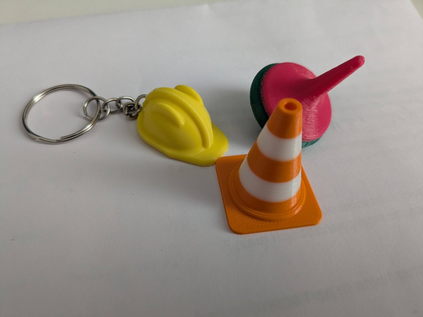 Gros plan sur 3 impressions 3D : un casque de chantier jaune, un cône de signalisation et une toupie.