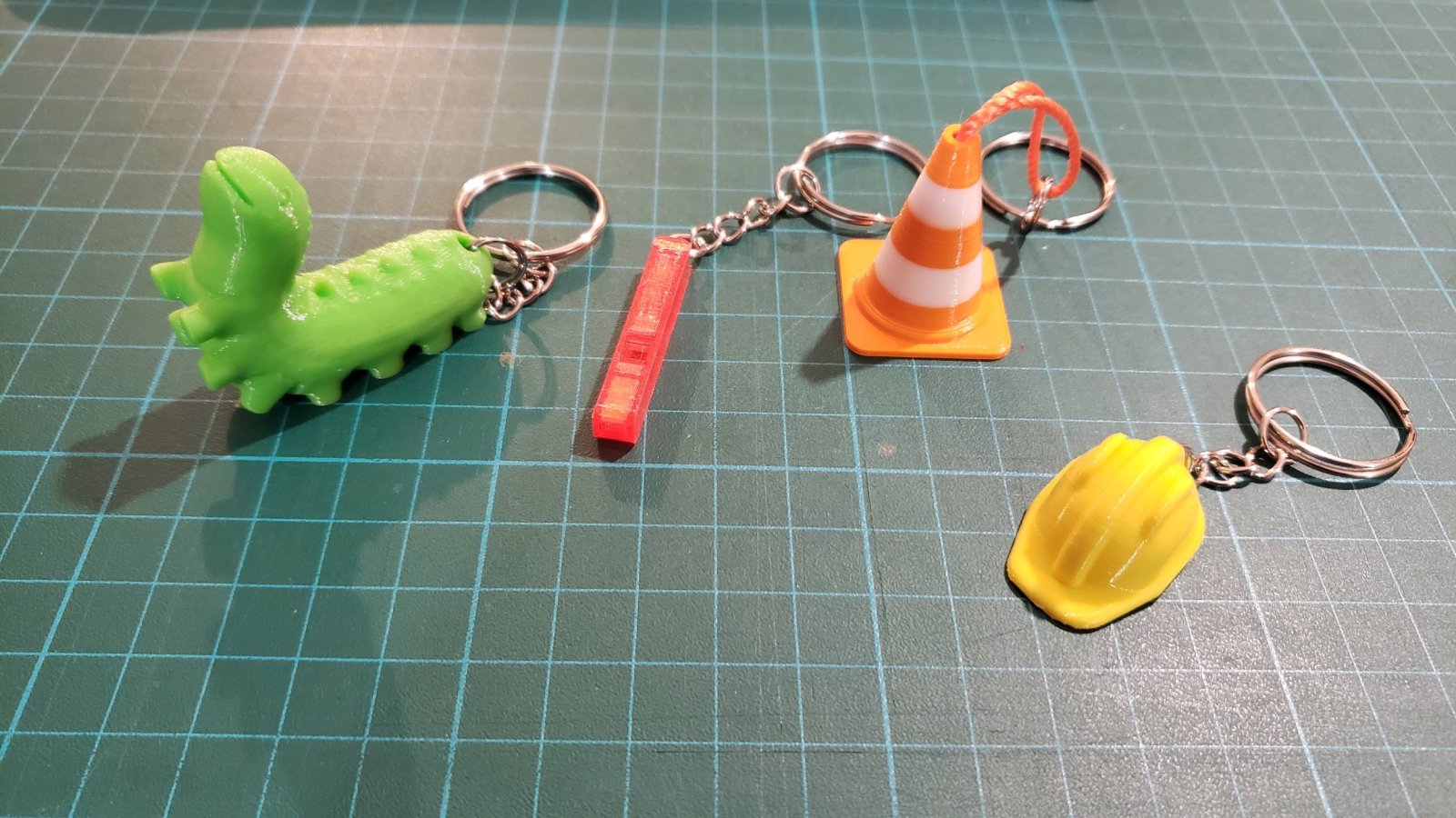 4 portes clés imprimés en 3D : une chenille, un sifflet, un cône et un casque de chantier.